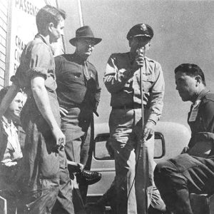 Group of white men, one in military uniform speaking into microphone