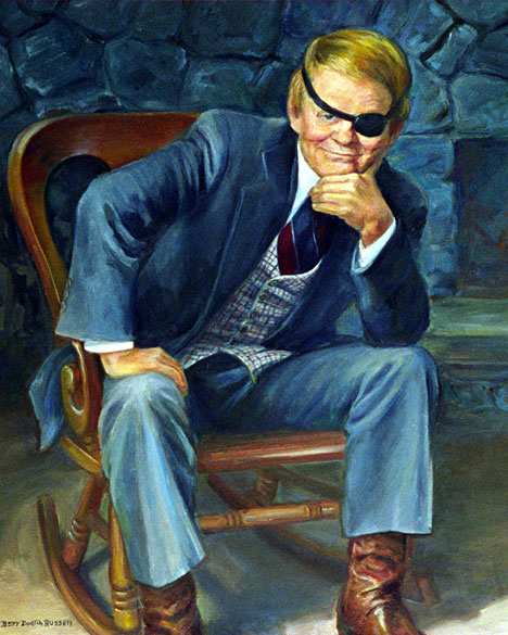 White man with eye patch in a suit sitting in a chair with fireplace