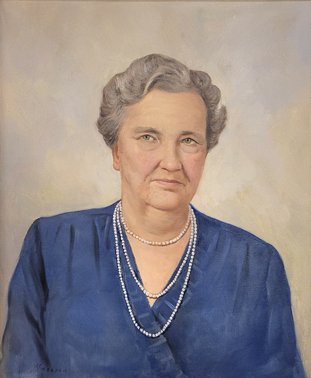 Older white woman with gray hair in blue with three strands of pearls