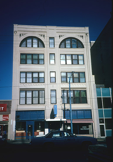 Five-story hotel building with arched windows on top floor and striped awing on first floor over the words "hotel restaurant" painted on front window