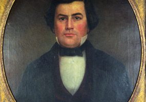 White man with dark hair in black suit and bow tie