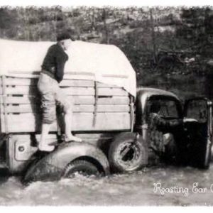 White man standing on truck in water with woman sitting in the passenger seat with her door open