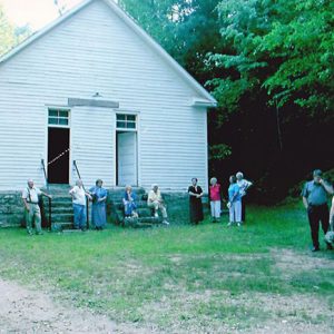 Group of older white men and women standing outside single-story building with two front doors