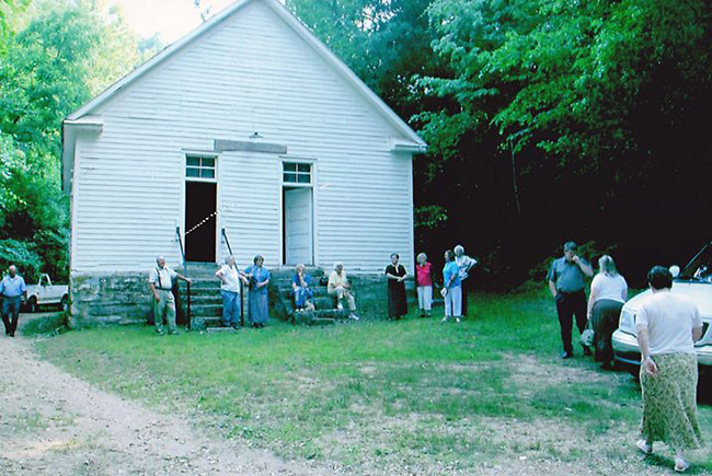 Group of older white men and women standing outside single-story building with two front doors