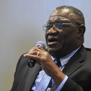African-American man with glasses in suit and tie speaking into microphone