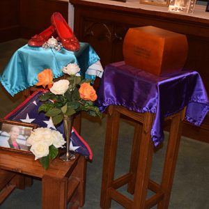 Red shoes urn and photograph with flag and flowers on wooden displays in church sanctuary