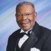 African-American man with mustache and glasses smiling in tuxedo