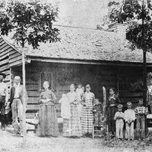 White men women and children standing outside house with covered porch