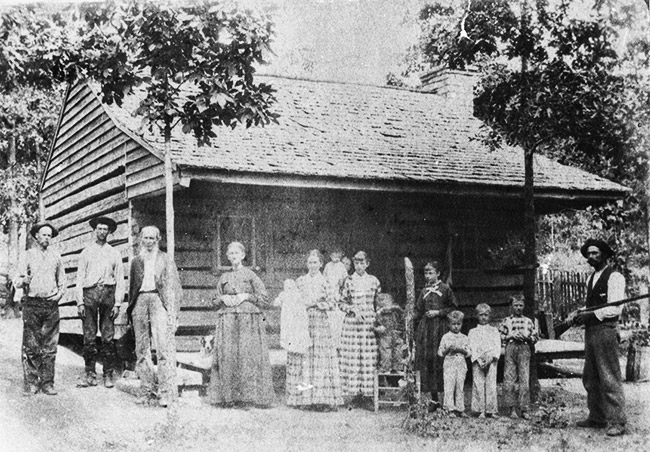 White men women and children standing outside house with covered porch
