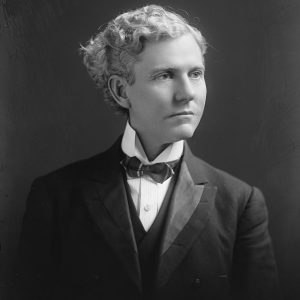 White man with curly hair in suit and bow tie
