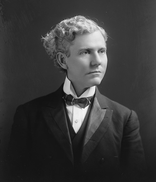 White man with curly hair in suit and bow tie