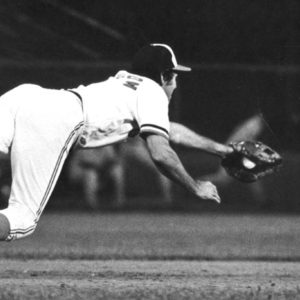 White man in baseball uniform catching a ball in midair