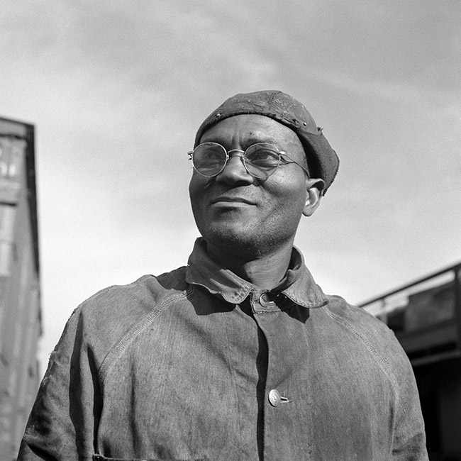 African-American man with glasses smiling in hat and button-up shirt