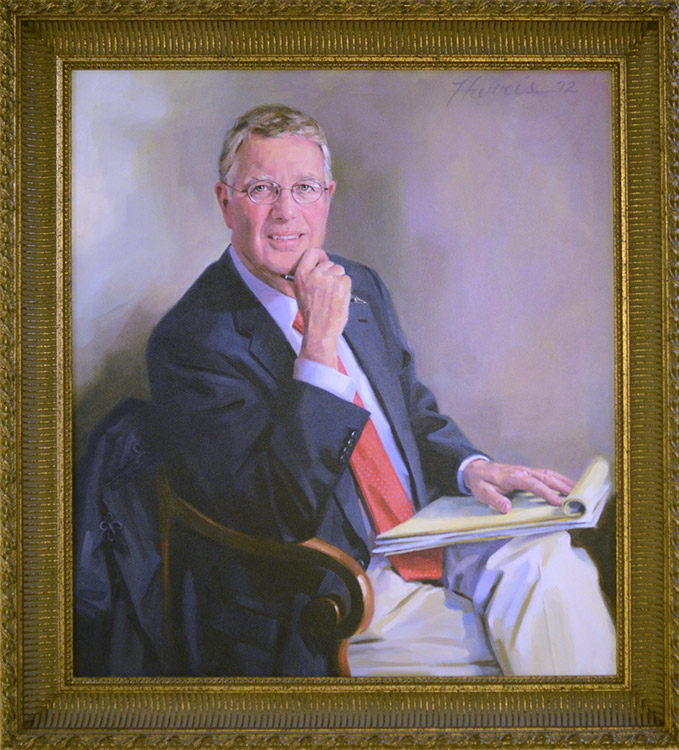 White man in suit and glasses sitting with notepads