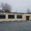Single-story brick storefront with "Rock Town Distillery" painted above three large windows and parking lot
