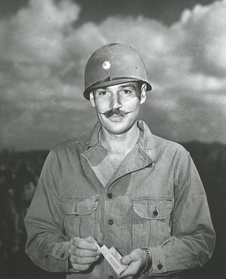 white man with mustache in military uniform with helmet holding a pack of cigarettes