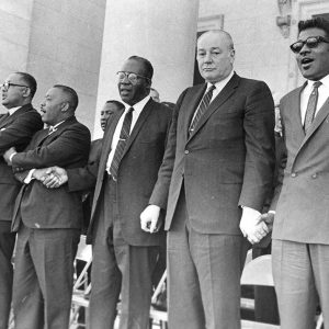 African-American men in suits and white man in suit holding hands on capitol building steps