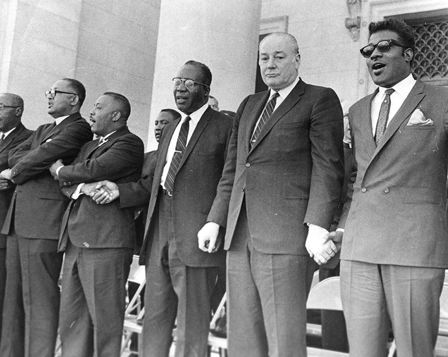 African-American men in suits and white man in suit holding hands on capitol building steps