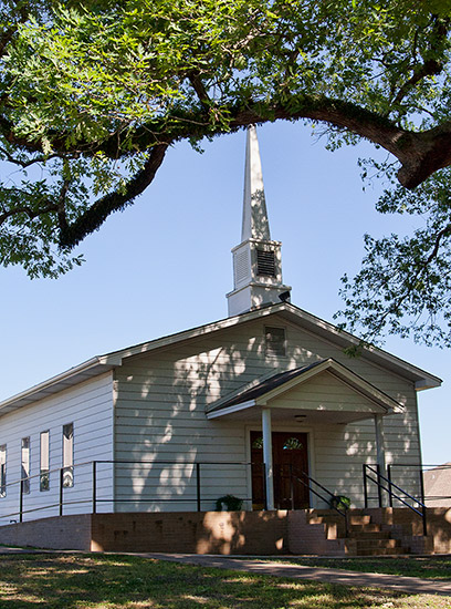 Single-story white church building with steeple and tree