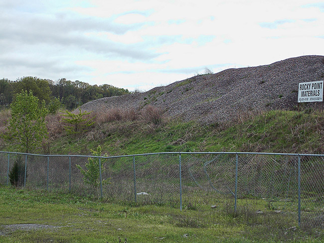 Grass covered mound with "Rocky Point Minerals" sign on it inside fence