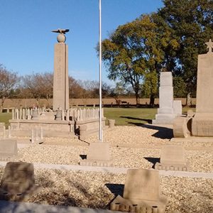 Group of stone monuments on gravel with flag pole in field