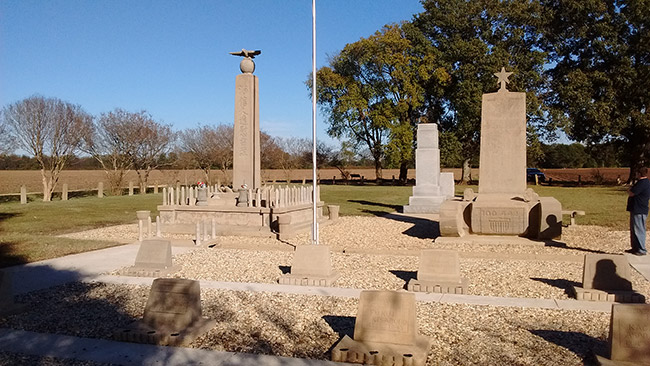 Group of stone monuments on gravel with flag pole in field