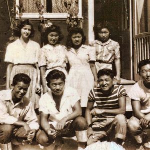 White woman standing with three Japanese-American women and four Japanese-American men kneeling in front of them