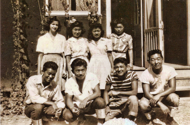 White woman standing with three Japanese-American women and four Japanese-American men kneeling in front of them