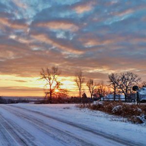 Snow covered road with tire tracks at sunset looking toward the sun