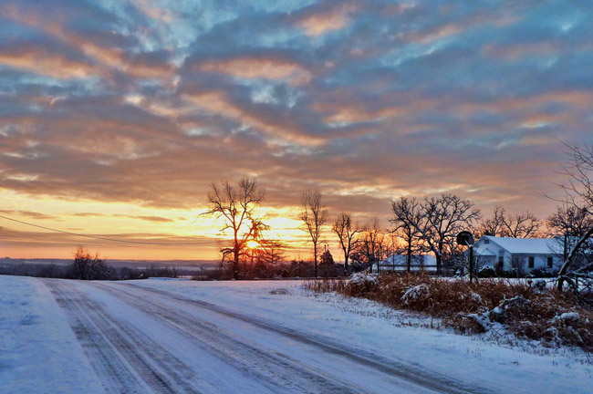 Snow covered road with tire tracks at sunset looking toward the sun