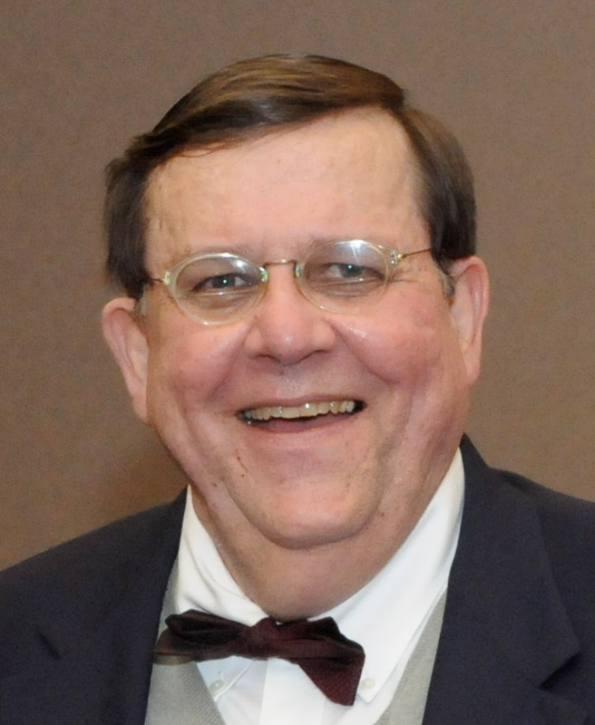 White man with glasses smiling in suit and bow tie