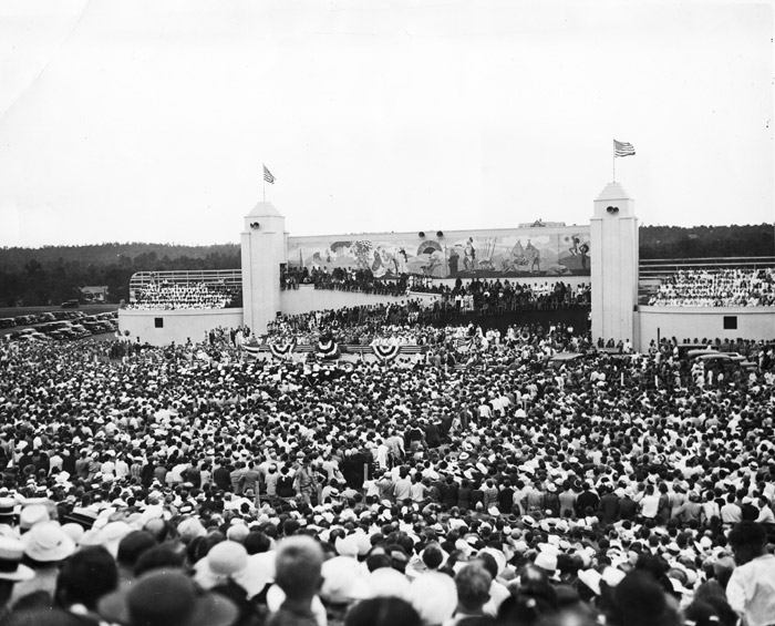 large crowd fills stadium, platform decorated with banners in the distance