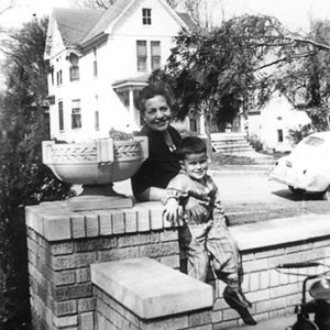 Older white woman with boy on brick wall with car and house in the background