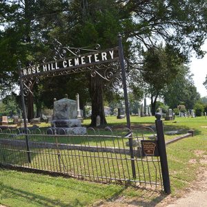 "Rose Hill Cemetery" sign and fence with gravestones beyond it