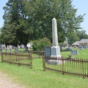 Family plot with iron fence and rows of gravestones in cemetery