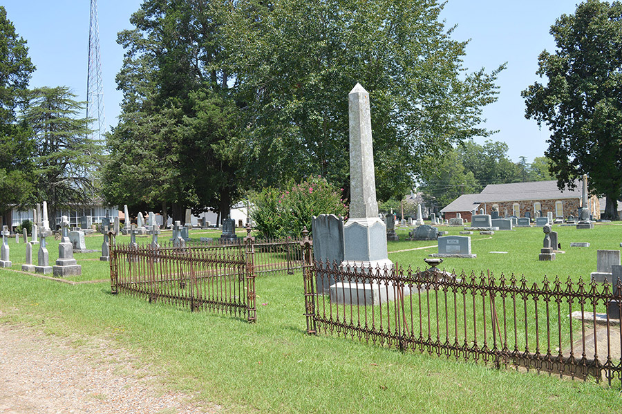 Family plot with iron fence and rows of gravestones in cemetery