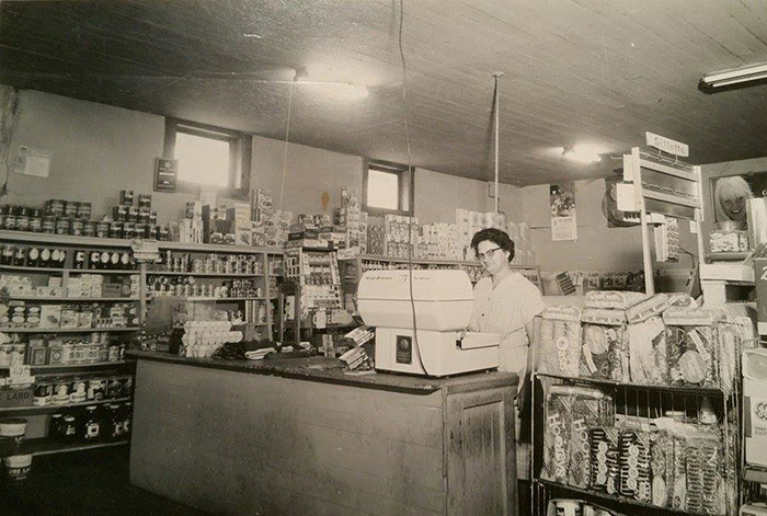 White woman with glasses sitting behind the counter in general store