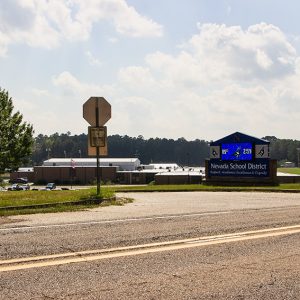 View from two-lane road of gymnasium and single-story buildings with electronic sign in the foreground