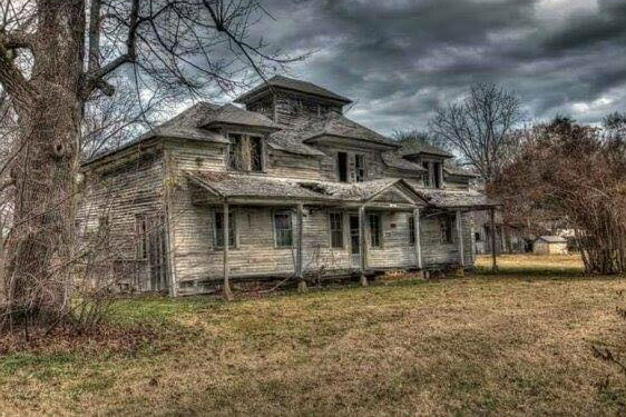Abandoned multistory house with covered porch under cloudy skies