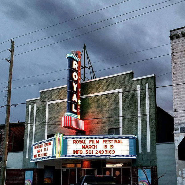 Multistory theater building with lit neon sign and marquee on street at night