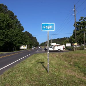 Two-lane highway next to green "Royal" road sign with white truck on road behind it