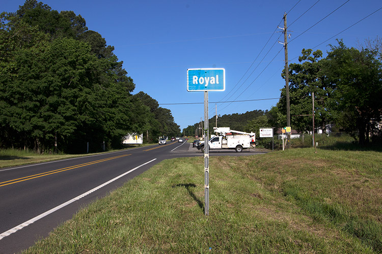 Two-lane highway next to green "Royal" road sign with white truck on road behind it