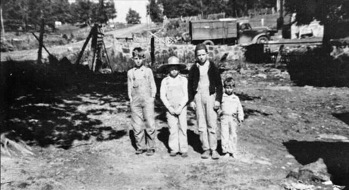 Four white boys standing with truck and stone wall behind them