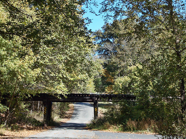 Side view of railroad bridge over rural road surrounded by trees