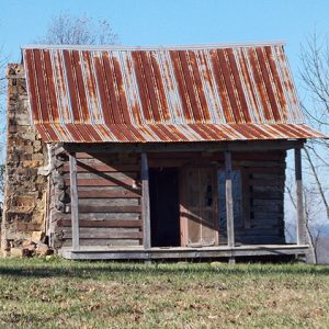 Abandoned log cabin with rusted metal roof and covered porch and stone chimney