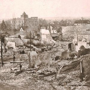 Ruins of burned down buildings with town buildings in the background