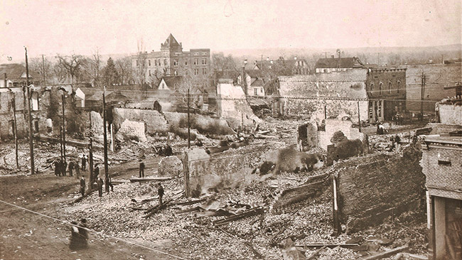 Ruins of burned down buildings with town buildings in the background