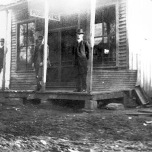 White men in hats standing outside a building with a dirt road