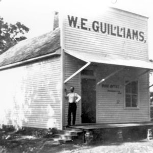 White man standing outside "W. E. Guilliams" post office