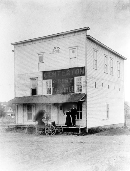 Three-story building labeled "Centerton Grist & Feed Mill" with two people and wagon in front of it